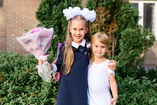 portrait of a cute little seven year old first-grader girl with a bouquet of flowers with her younger brother ready to go to school. back to school concept