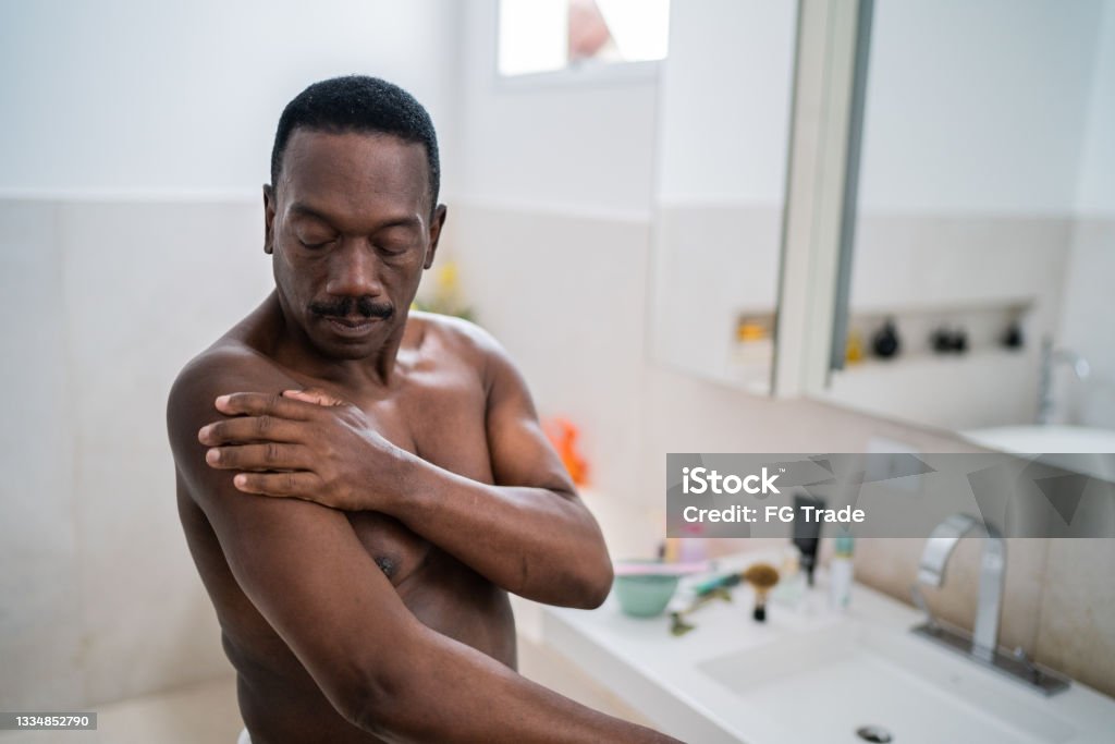 Senior man applying moisture on body at home Moisturizer Stock Photo