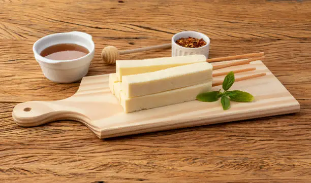 Rennet or Coalho cheese on a wooden board with sugar syrup and pepper.