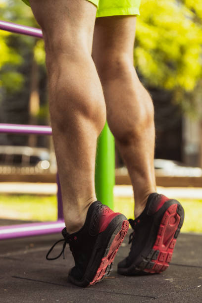 Cropped image of male muscular legs, feet in sportshoes standing on tiptoes during sports training outdoors Muscular build. Cropped image of male legs, feet in sportshoes standing on tiptoes during sports training outdoors. Concept of doing sports, fitness, well-being tiptoe stock pictures, royalty-free photos & images