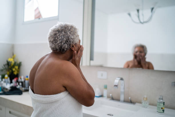Senior woman applying body moisture in the bathroom at home