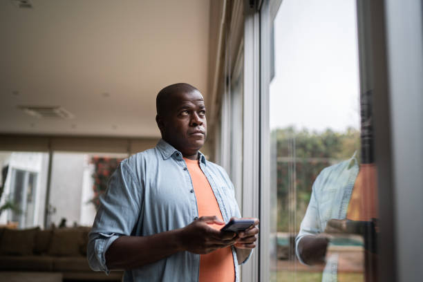 men contemplating holding a smartphone at home - waiting telephone on the phone anxiety imagens e fotografias de stock