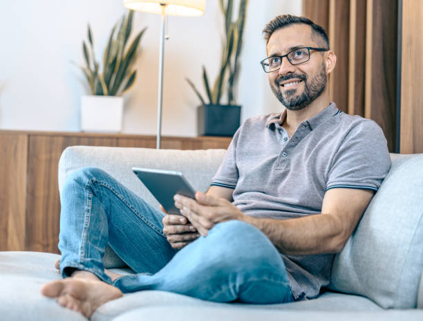 istock Middle aged man sitting on sofa, reading on tablet 1334856345