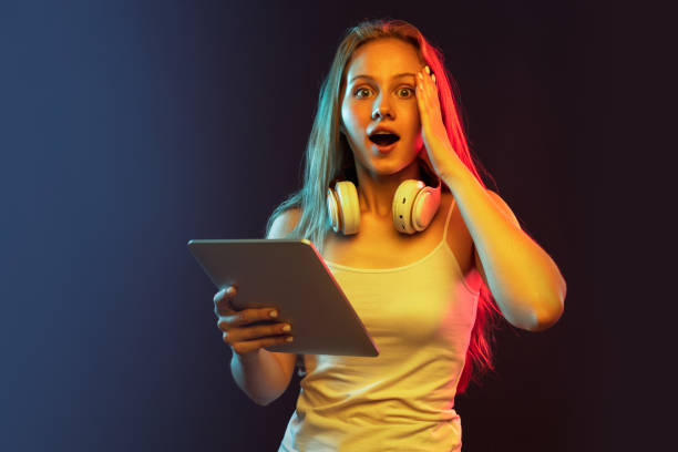 istock Portrait of young beautiful girl using tablet isolated on dark blue studio background. Concept of human emotions, facial expression, youth, sales, ad , gadgets 1334856475