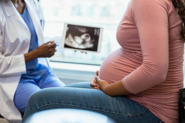 Focus on foreground as doctor shows ultrasound in background A photo with the focus on the unrecognizable pregnant woman in the foreground as the unrecognizable doctor shows her an ultrasound on a digital tablet in the background. ultrasound photos stock pictures, royalty-free photos & images