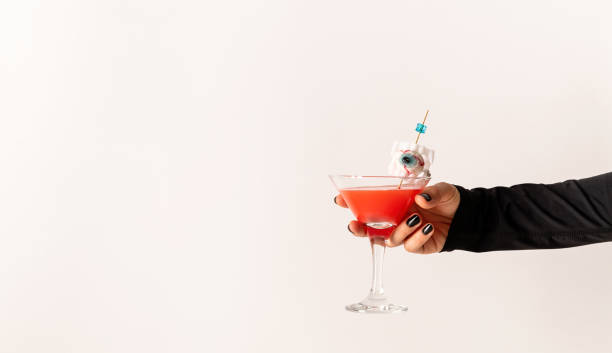 白い背景に怖い赤いハロウィーンのカクテルとガラスを保持している黒い爪を持つ女性の手 - glass autumn halloween food ストックフォトと画像