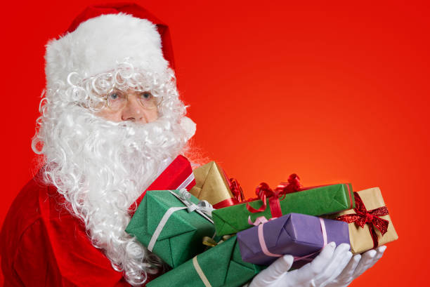 istock Happy Santa Claus with gift boxes in hands on red background with copy space 1334865544