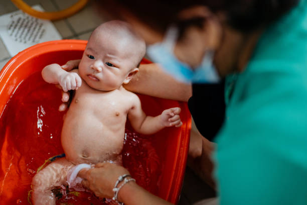 Image of an Asian grandmother taking a bath for her grandson in bathroom. Woman clean her baby's body with cloth and warm water.