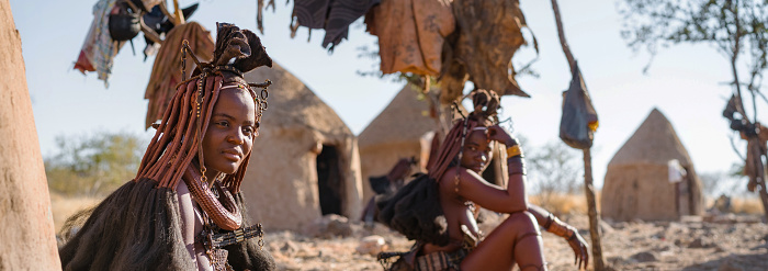 Panoramic shot showing Himba women sitting outside their huts in a traditional Himba village near Kamanjab in northern Namibia, Africa.