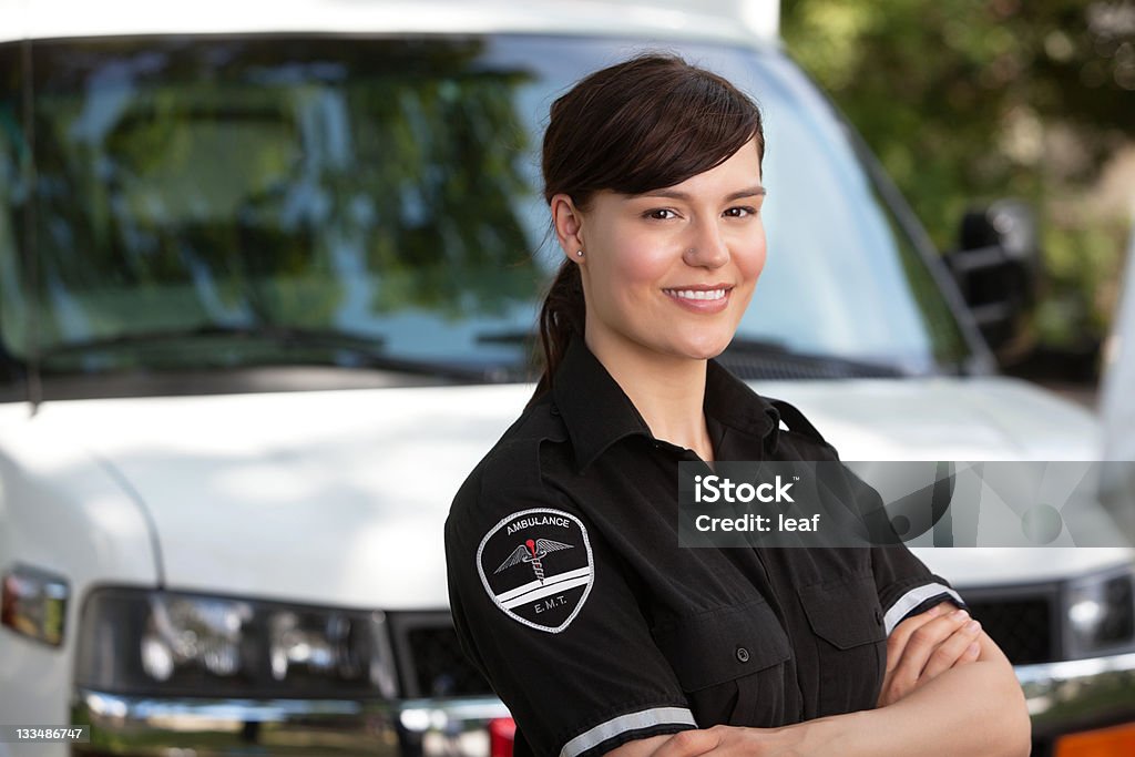 Female paramedic standing outside of her ambulance Portrait of a happy friendly female paramedic standing in front of ambulance Paramedic Stock Photo