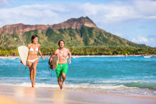 gente de surf feliz divirtiéndose surfeando en la playa de waikiki, honolulu, oahu, hawai. mujer asiática, hombre caucásico pareja multirracial que se que acaba de agua salpicaduras del océano. vacaciones de verano paisaje de viajes - waikiki beach fotografías e imágenes de stock