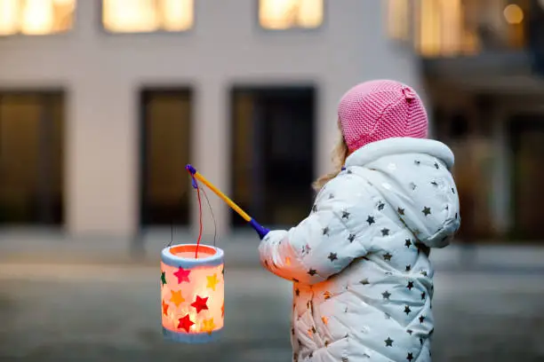 Little kid girl holding selfmade lanterns with candle for St. Martin procession. Healthy cute toddler child happy about children and family parade in kindergarten. German tradition Martinsumzug.