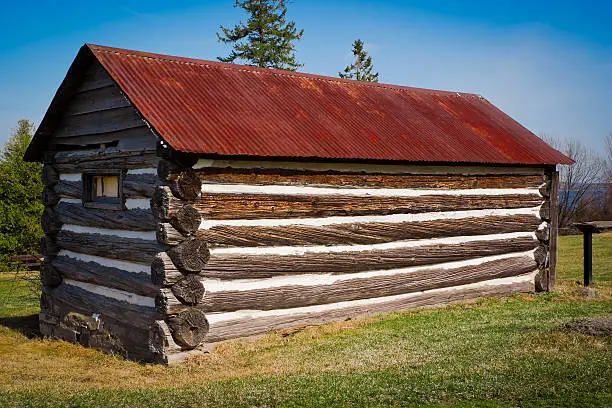 A very small, but long, old log cabin with rusted tin roof at Pinhey's Point historical park near Ottawa, Ontario Canada.