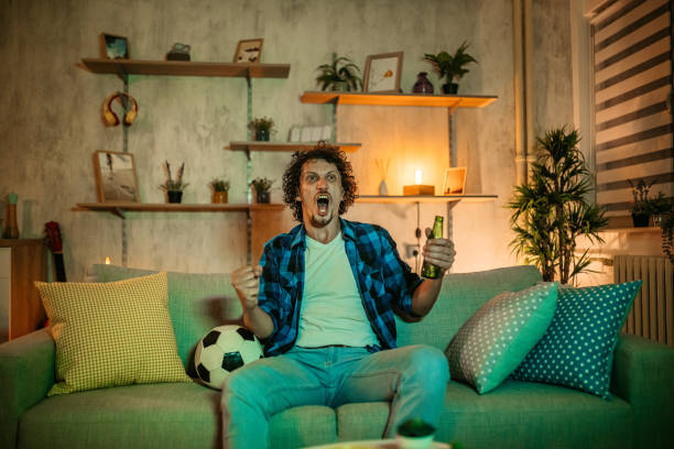 Man watching soccer match on TV Handsome young man watching soccer match on TV at home in the evening and drinking beer. He is celebrating win of his team. bachelor stock pictures, royalty-free photos & images