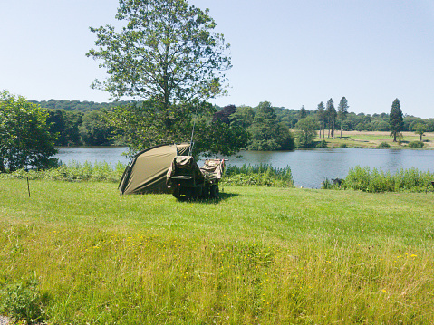 Gone fishing -tent and fishing rods set up overlooking beautiful lake in rural UK on a sunny summers day so that fisherman can enjoy his hobby overnight as well as in the day light hours.
