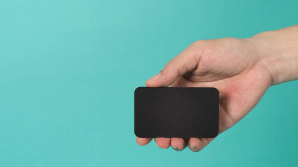 istock Empty space for text.Male hand holding black blank card isolated on mint green or Tiffany Blue background. 1334886552