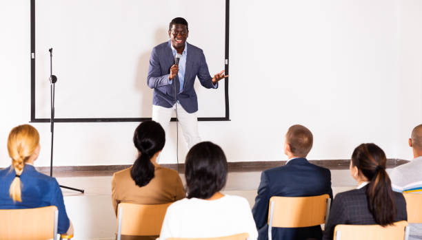 istock Expressive african american speaker with microphone on conference room stage 1334888639