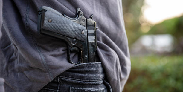 Gloved hand carrying a pistol in his pants, blur nature background, Armed man carrying a pistol in his jeans waistband, blur outdoor nature background. Threat, violence and danger concept gunman photos stock pictures, royalty-free photos & images