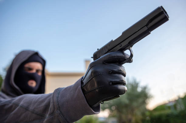 istock Hooded robber holding a pistol, blur nature background, 1334890765