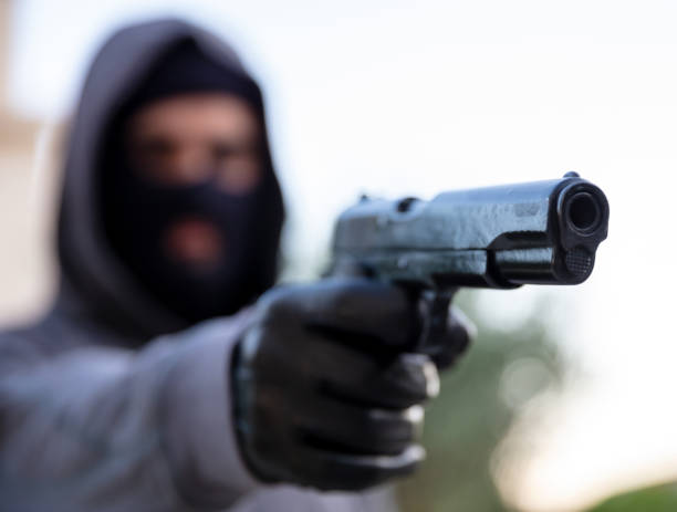 istock Hooded thief holding a pistol, blur nature background, 1334890766