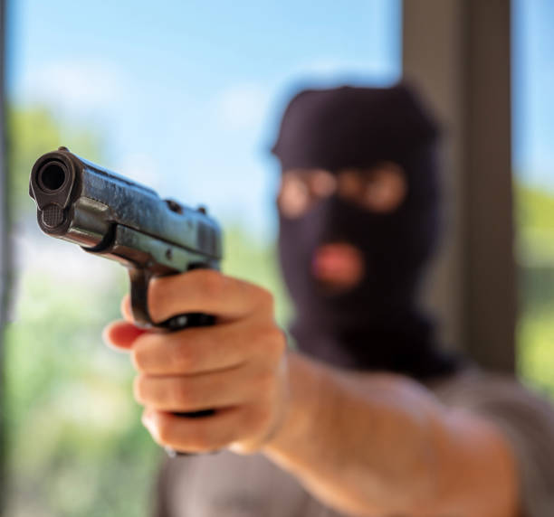 istock Hooded robber hand holding a pistol, blur background, 1334890772
