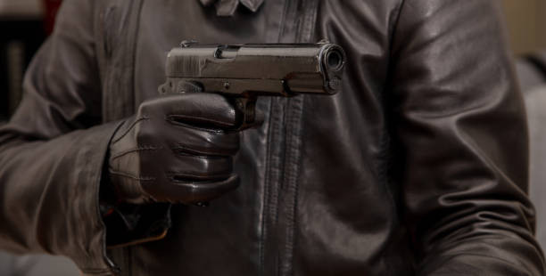 Gloved hand holding a pistol aiming, closeup view Pistol in gloved hand. Killer, murderer wearing black leather jacket aiming with a gun closeup view. Armed robbery, gunman concept forty five caliber handgun stock pictures, royalty-free photos & images