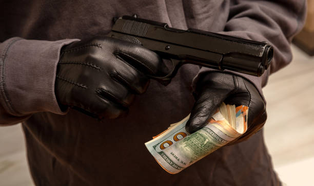 istock Gloved hand holding a pistol stealing money, closeup view. Armed robbery concept 1334890796
