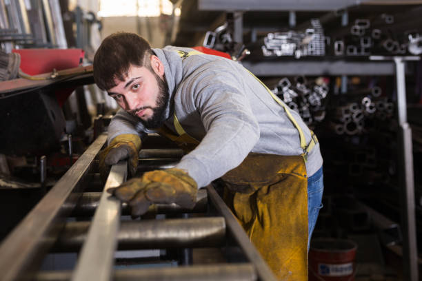 Blacksmith controlling quality of metal parts Portrait of young focused blacksmith during daily work in metalworking factory controlling quality of metal parts metal worker stock pictures, royalty-free photos & images