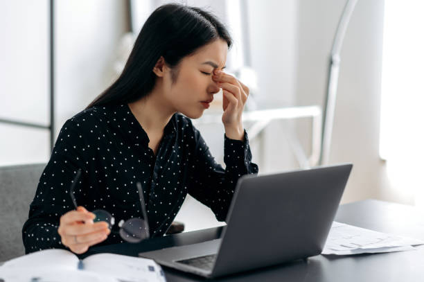 istock Overworked sad asian young woman, freelancer or manager, tired working using laptop, sitting at workplace. Upset girl rubbing nose bridge, holding eyeglasses in hand, closes eyes 1334894907
