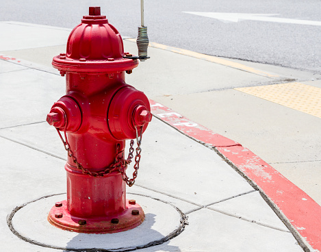 Red fire hydrant on top of a mountain in San Jose, California. There are wild plants on the side and a view of the mountains and sky at the background.