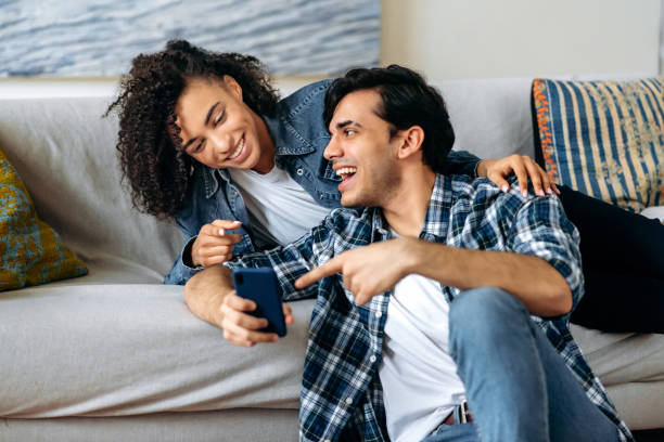 istock A loving young multiracial couple spends leisure time at home on the sofa, using a smartphone, browsing the Internet and social networks, laughing, the guy shows the girl something funny on the phone 1334901491