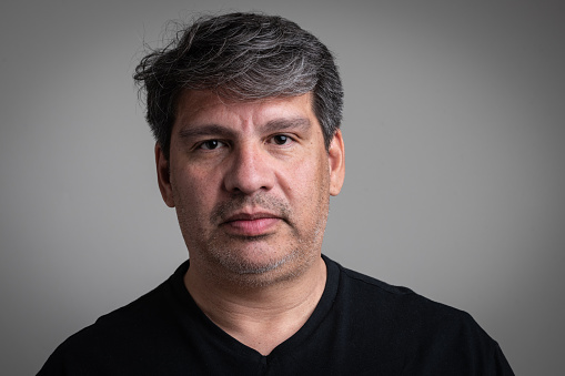 Pensive Hispanic mature man looking at the camera on gray background