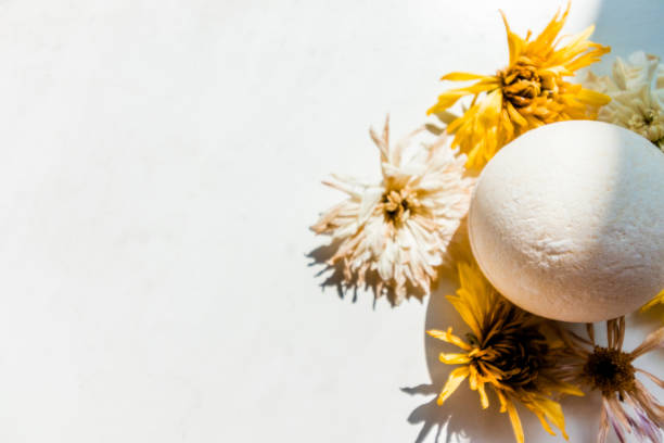 White bath bomb among dried flowers on a white background. Nursing bath procedures. Beauty industry.