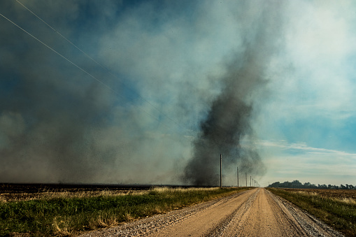 A landscape shot of a dust devil, wind whirl, or dust whirl of dust swirling in a swirl over power lines and a dirt road in a rural scene
