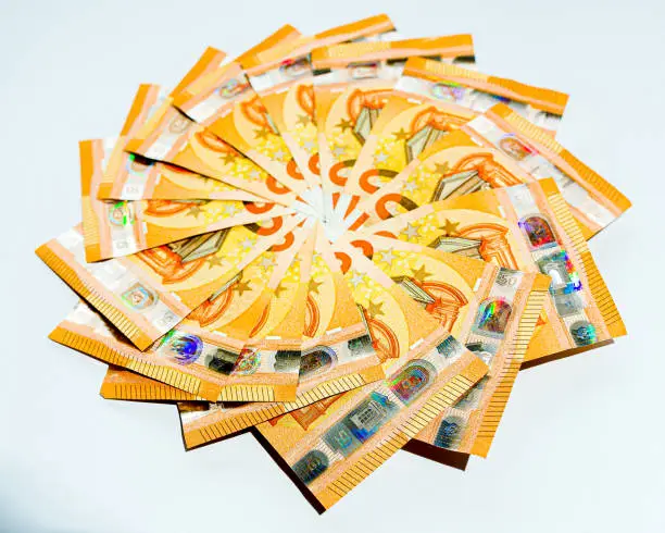 A view of a series of €50 euro notes in a spiral with the numbers in the white boxes edited out and the whole note is not visible with the hologram section being the only fully visible section of the notes.