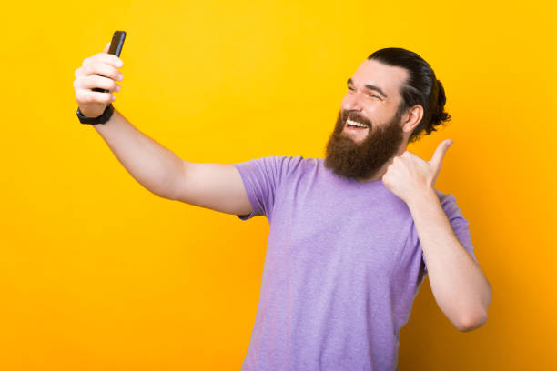 istock Wide smiling young man is making a selfie over yellow background. 1334908303