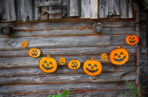 Halloween decoration outdoors. Paper garland with cute pumpkins hanging on the wooden wall of the old bathhouse building in village.