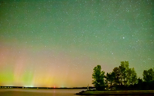Green pink and yellow aurora borealis over Lake Simcoe in starry sky at night