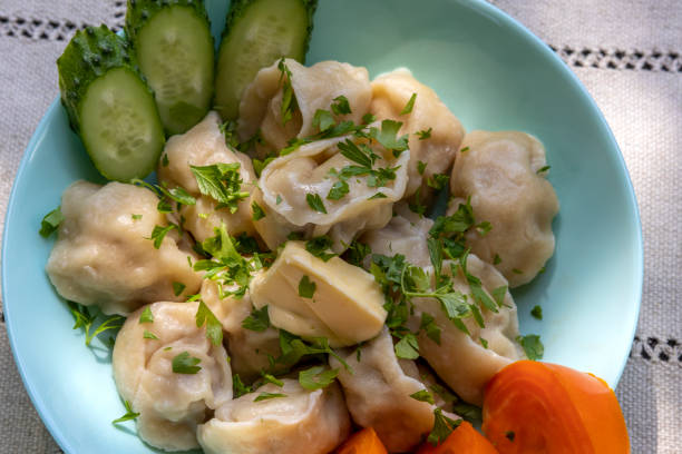 Dumplings stuffed with minced meat. With butter and herbs Pelmeni stuffed with minced meat. Decorated with chopped parsley, slices of fresh cucumber and yellow tomato. Topic - home-made food russian pelmeni stock pictures, royalty-free photos & images