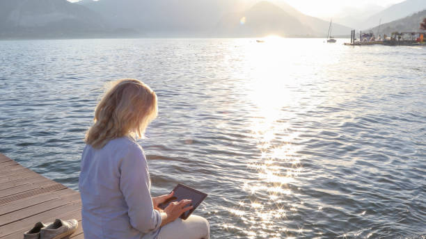 istock Woman relaxes on dock and uses digital tablet, at sunrise 1334920664