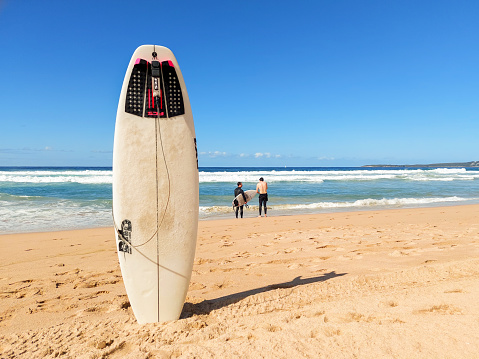 Cronulla, Australia - August 18, 2021: Wanda beach with old surfboard and two young friends surfers standing on edge of ocean and talking