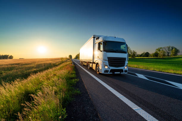 camion bianco che guida sulla strada asfaltata nel paesaggio rurale al tramonto - truck horizontal shipping road foto e immagini stock