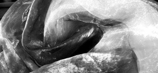 istock Organza. Shiny, reflective, beautiful fabric for curtains, tulles. Interior design option. Twisted, casually folded organza section in sunlight. black and white, monochrome, Banner 1334931992