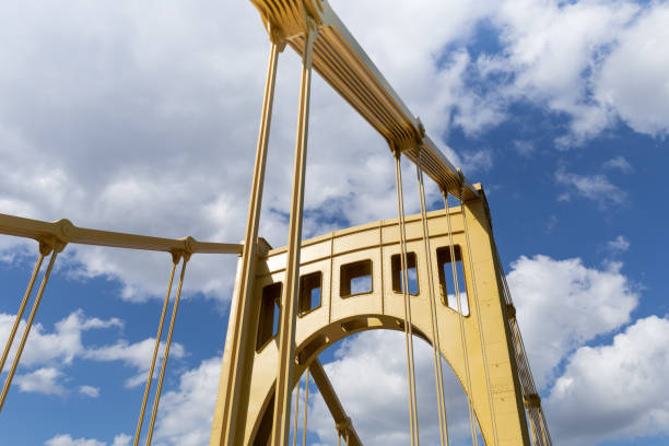 istock Bright sunlight on the upright structure of a yellow self anchored suspension bridge, deep blue sky with clouds 1334940352
