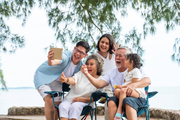 szczęśliwa wielopokoleniowa azjatycka rodzina korzystająca z cyfrowego tabletu wideo z przyjacielem rodziny na plaży - father digital tablet asian ethnicity daughter zdjęcia i obrazy z banku zdjęć