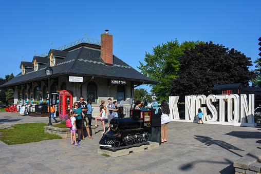 Kingston, Canada - August 15, 2021: The Kingston Ontario Visitor Information Centre, formerly a train station, with a sign for tourists to pose with, a model train and a vintage steam locomotive to remind people the city was once home to the Canadian Locomotive Company