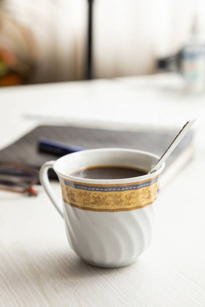 beautiful porcelain cup with coffee and a spoon inside, on a desk with glasses, a notebook and pen, drinks in the workplace, studio