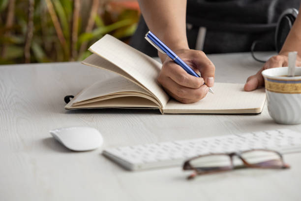 istock hand of a person who is writing with a pen on a notebook, workplace with glasses, computer mouse, and keyboard. office supplies in studio 1334941862