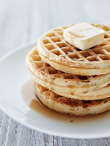 A stack of waffles with butter and syrup on a plate.