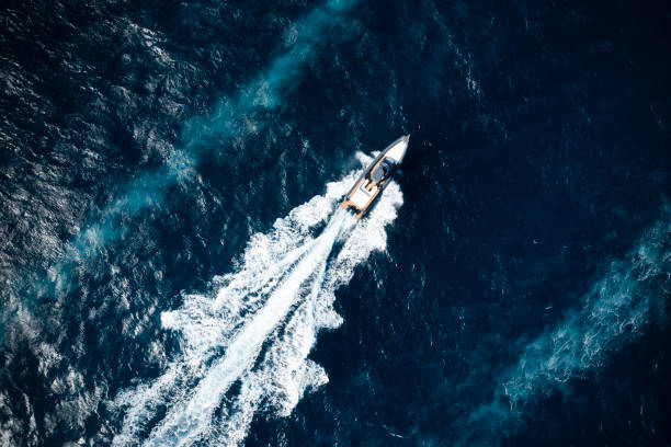 View from above, stunning aerial view of a boat cruising on a blue water creating a wake. Costa Smeralda, Sardinia, Italy. stock photo